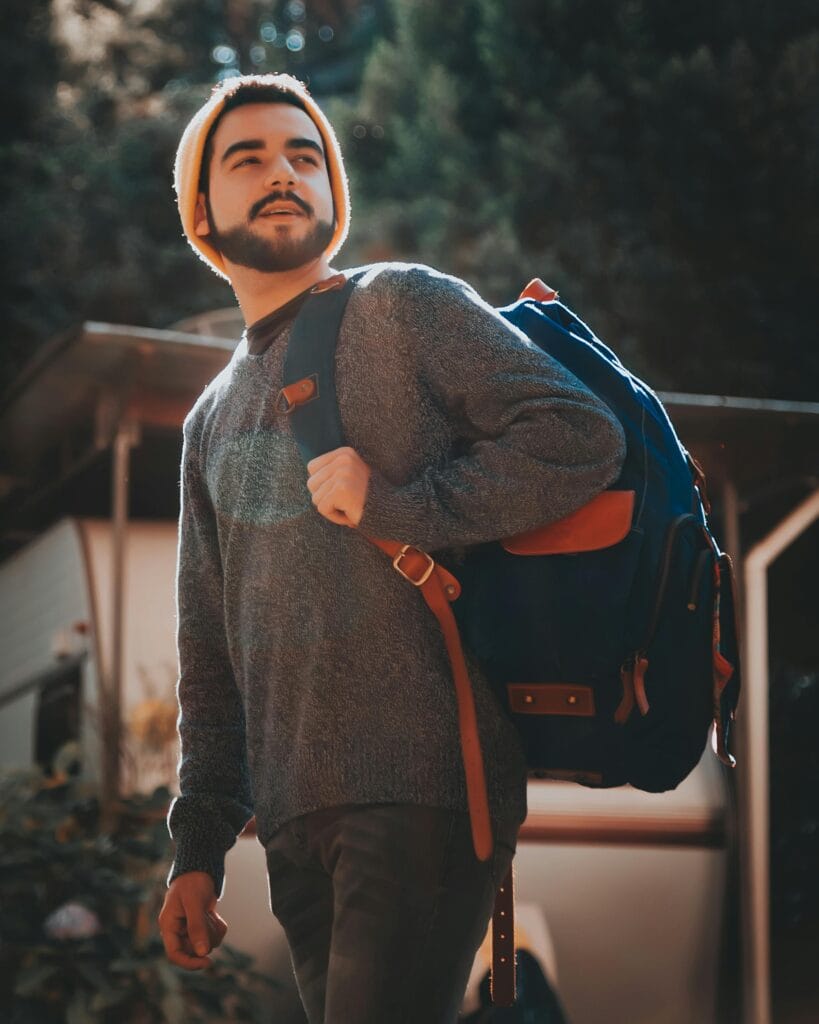 A fashionable man poses with a backpack in a sunny outdoor setting in São Paulo, Brazil.